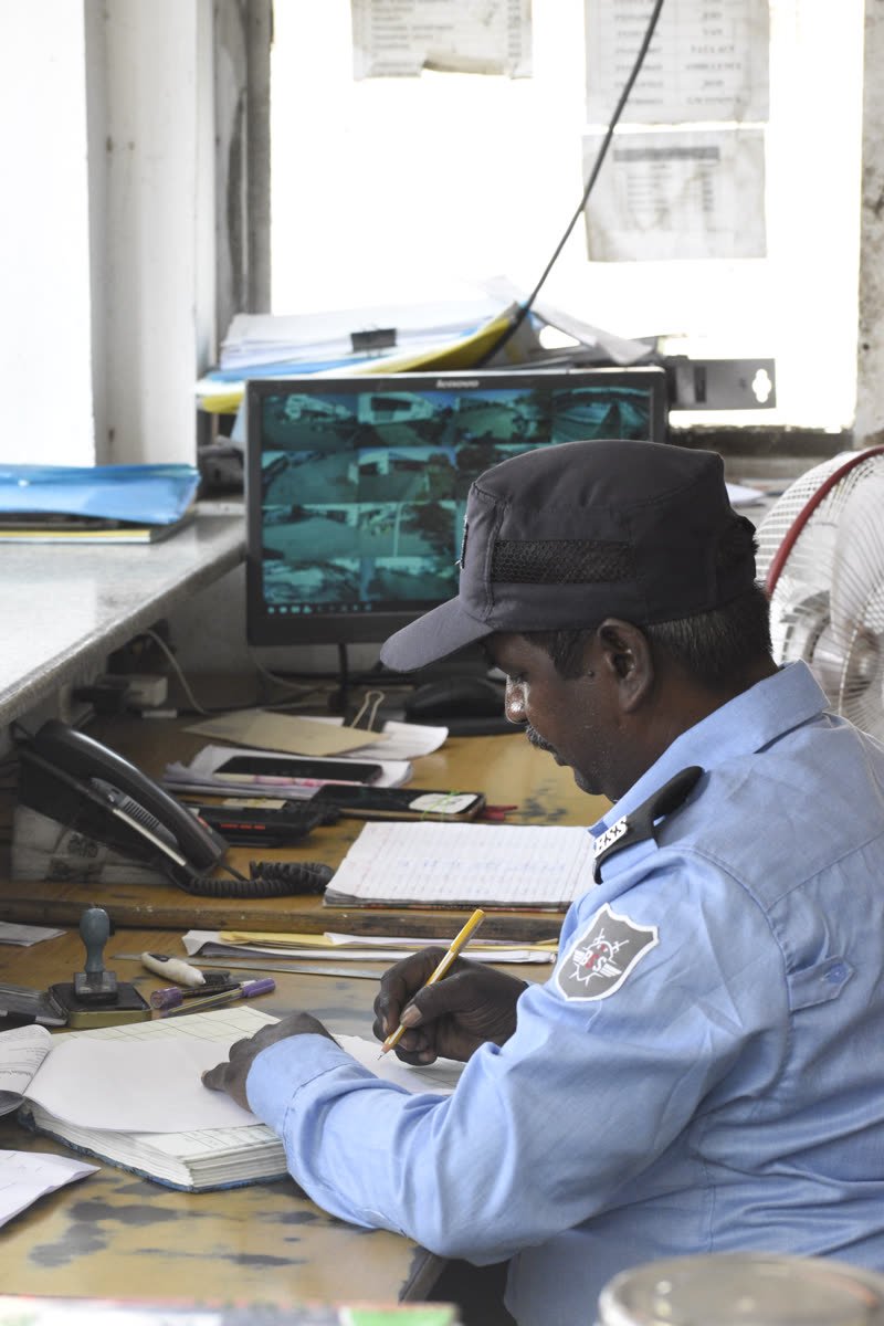 A BSS guard writing in the duty register beside a CCTV monitor